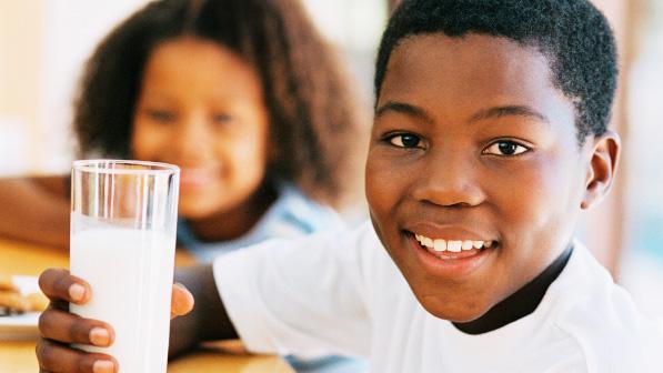 A smiling boy sitting drinking his glass of milk