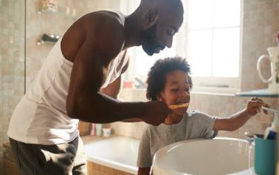 A father helping his kid to brush his teeth